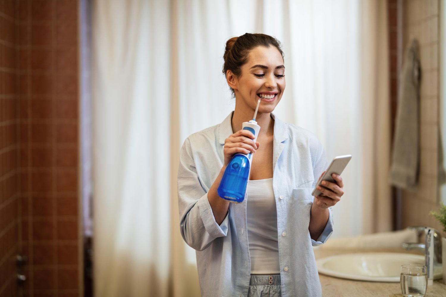Frau mit Munddusche und Smartphone in der Hand