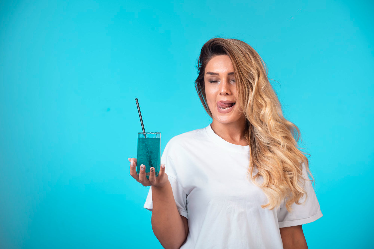 Junges Mädchen im weißen Hemd hält ein Glas mit blauem Cocktail in der Hand und spürt den Geschmack.