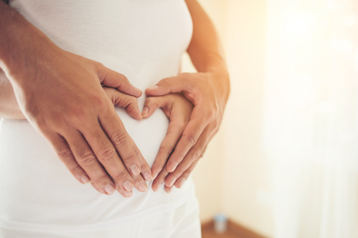 Schwangere Frau und ihr Partner mit Händen herzförmig auf dem Bauch