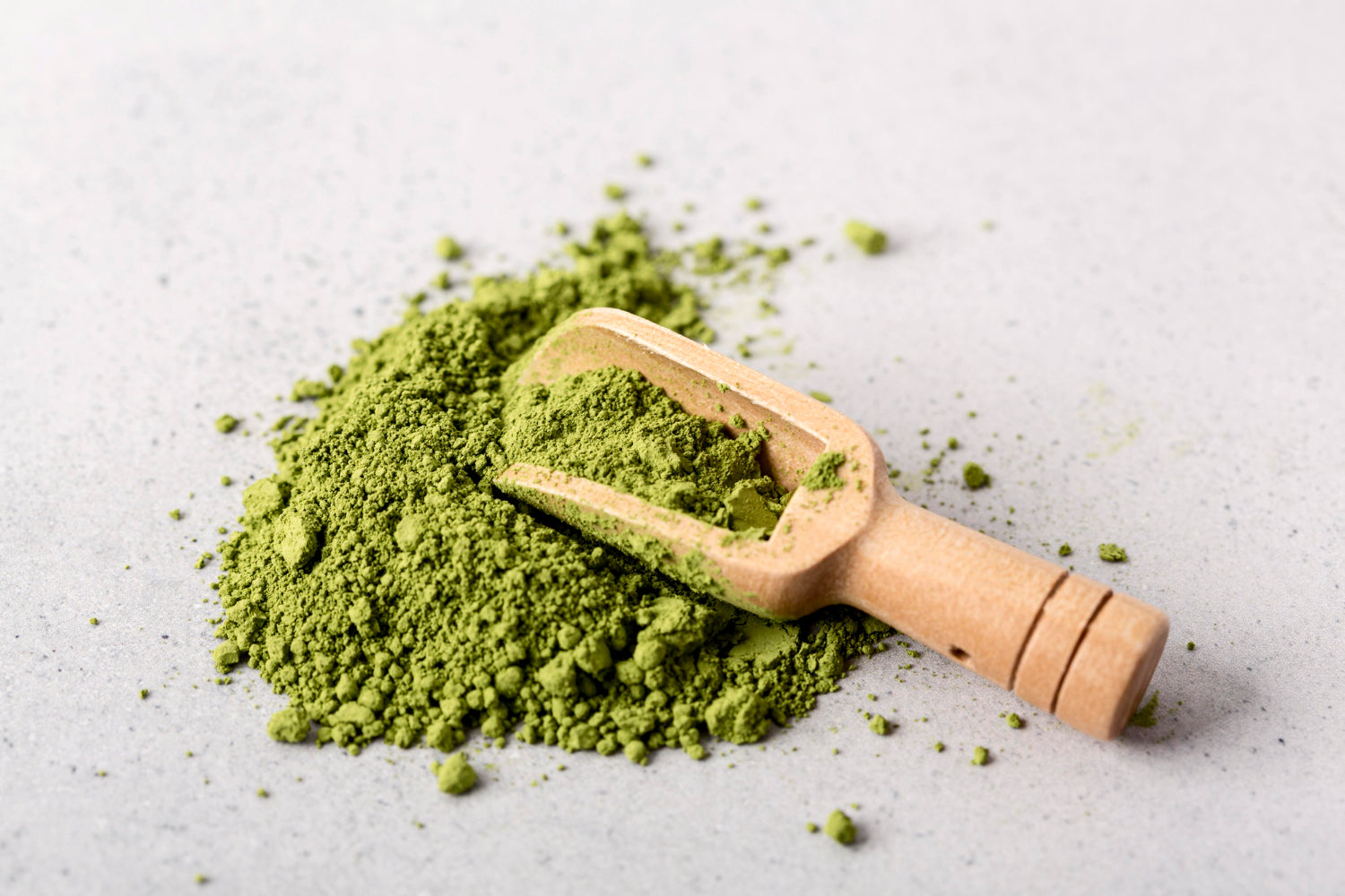 ChatGPT:  DasMatcha-Tee Pulver auf einer hellen Oberfläche, mit einem kleinen Holzschäufelchen darin.