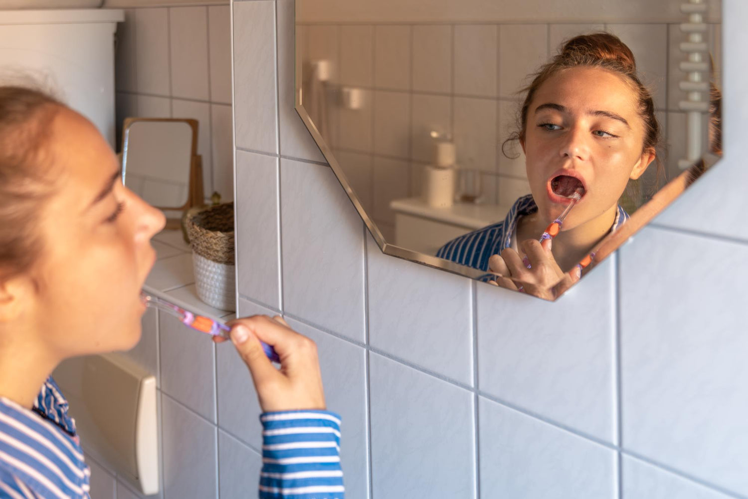 Mädchen putzt sich vor dem Spiegel im Badezimmer die Zähne.