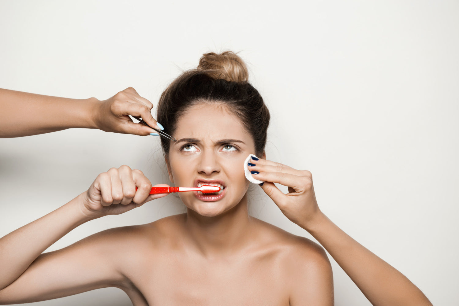 Eine Frau wirkt gestresst, während sie gleichzeitig Zähne putzt, ihre Augenbrauen zupft und ein Wattepad im Gesicht hält.